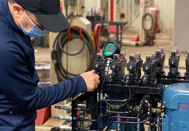 Technicien ajuste des valves sur une unité hydraulique avec manomètres dans un atelier industriel.