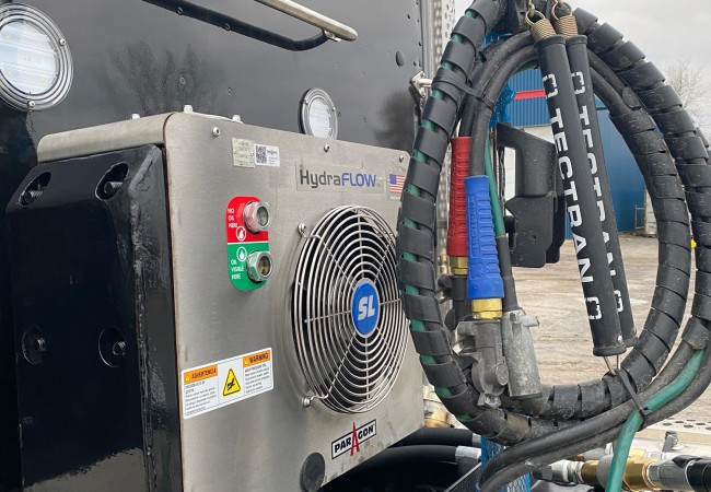 Un système HydraFLOW SL installé sur un camion noir avec des tuyaux et câbles attachés, sous un ciel nuageux.
