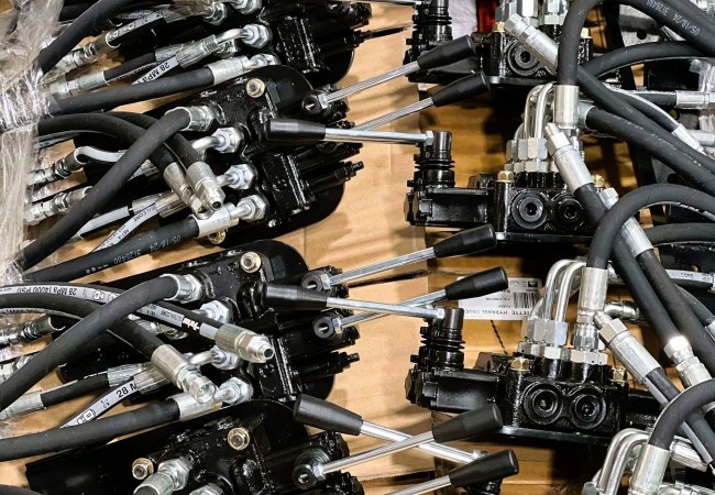 Plusieurs valves hydrauliques noires avec leviers métalliques et tuyaux flexibles sont disposées sur une surface en carton.