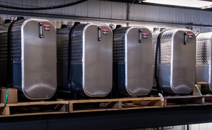Réservoirs en aluminium alignés sur une étagère métallique dans un entrepôt industriel avec des boîtes à droite.