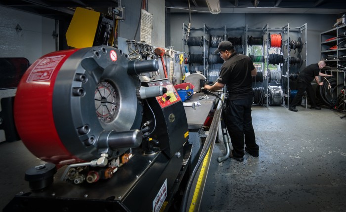 Atelier avec presse-boyaux hydraulique Parker au premier plan et deux techniciens travaillant sur des tuyaux.